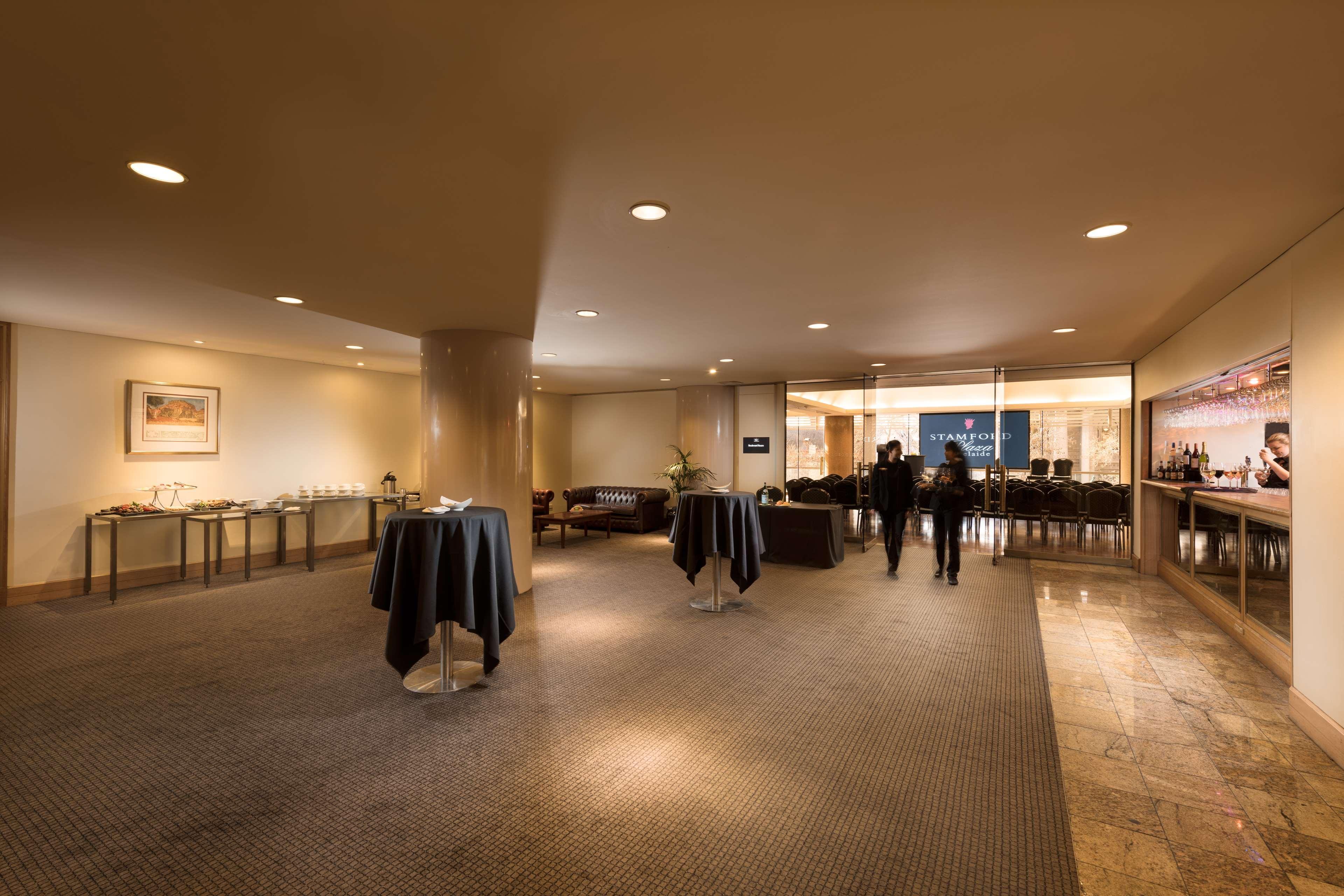 Hotel Stamford Plaza Adelaida Exterior foto The image shows an indoor space that appears to be a lounge or reception area. There are several round tables with dark tablecloths positioned throughout the room. The floor is carpeted, and the lighting is warm and somewhat dim. In the background, t